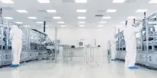 Operarios con trajes de protección blanca trabajando en una sala blanca industrial con maquinaria de alta precisión.