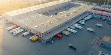 Vista aérea de un gran centro logístico con múltiples muelles de carga y camiones estacionados en un día soleado.