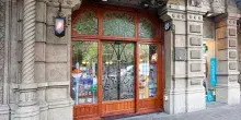 Entrada de madera de estilo modernista con vidrieras decorativas de motivos vegetales y columnas de piedra labrada.