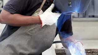 Operator performing welding work in an industrial environment for the manufacture of components for automatic doors.
