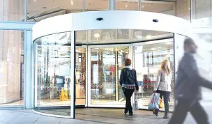 Puerta automática giratoria de cristal en la entrada de un centro comercial con personas entrando.