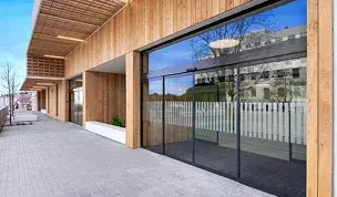 Fachada de madera moderna con una puerta automática corredera de cristal y franjas de seguridad horizontales.
