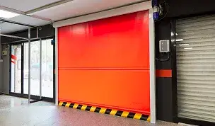 Porta rapida avvolgibile in telo rosso in un ambiente industriale con fascia di sicurezza inferiore rigata in giallo e nero.