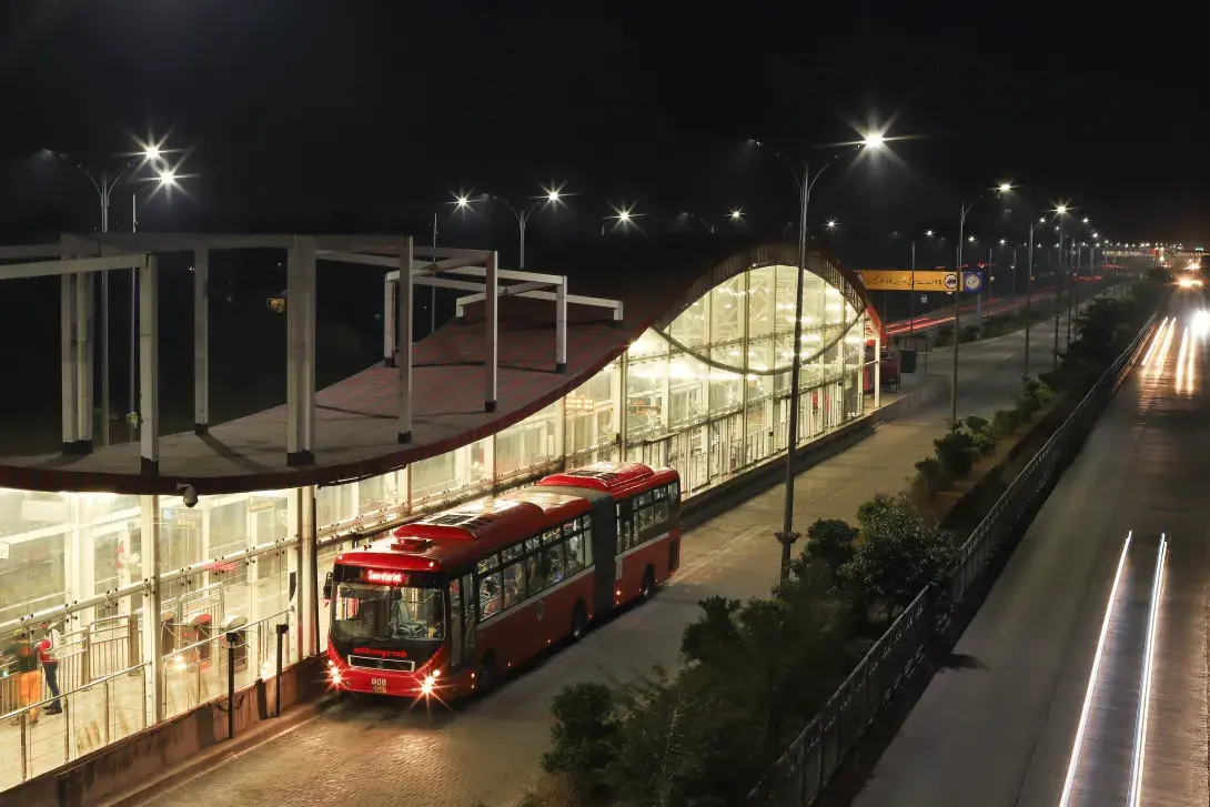 Autobús articulado rojo en una estación moderna del sistema BRT iluminada de noche.