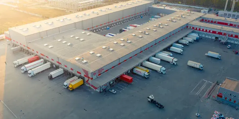 Vista aérea de un gran centro logístico con múltiples muelles de carga y camiones estacionados en un día soleado.
